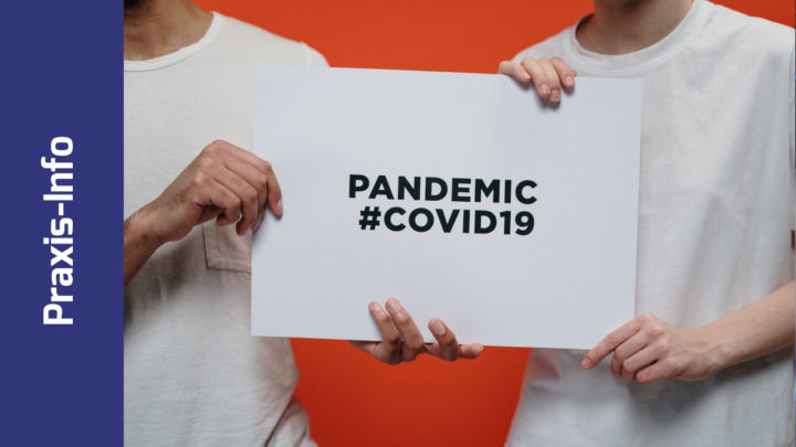 2 Personen halten ein Schild it der Aufschrift "Pandemic #COVID19"