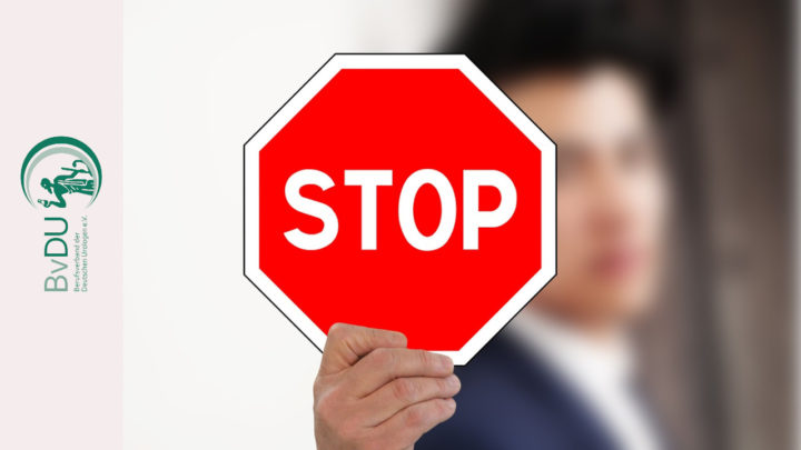 Ein Mann - schemenhaft im Hintergrund - hält ein Stop-Schild nach vorne