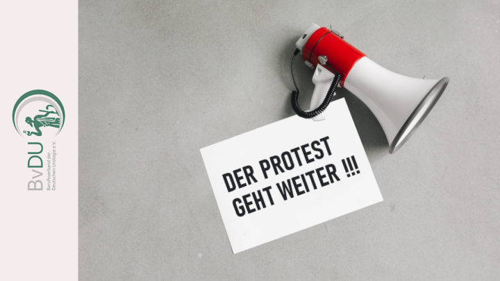 Ein Megaphone liegt auf einem Blatt Papier mit der Aufschrift: "DER PROTEST GEHT WEITER !!!"