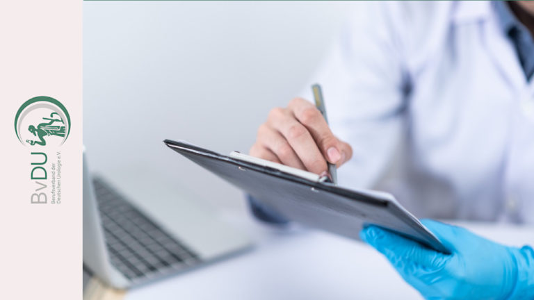 Ein Arzt sitzt bei einem Laptop und schreibt etwas auf ein Klemmbrett.