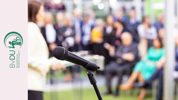 Kongress mit vielen Teilnehmern und Teilnehmerinnen im Hintergrund. Im Vordergrund ein Mikrofon