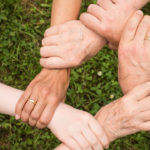 Fünf Personen fassen kreisförmig jeweils an das Handgelenk des nächsten.