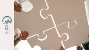 Blick von unten auf vier sehr große Puzzle-Teile, die von Händen zusammengehalten werden.