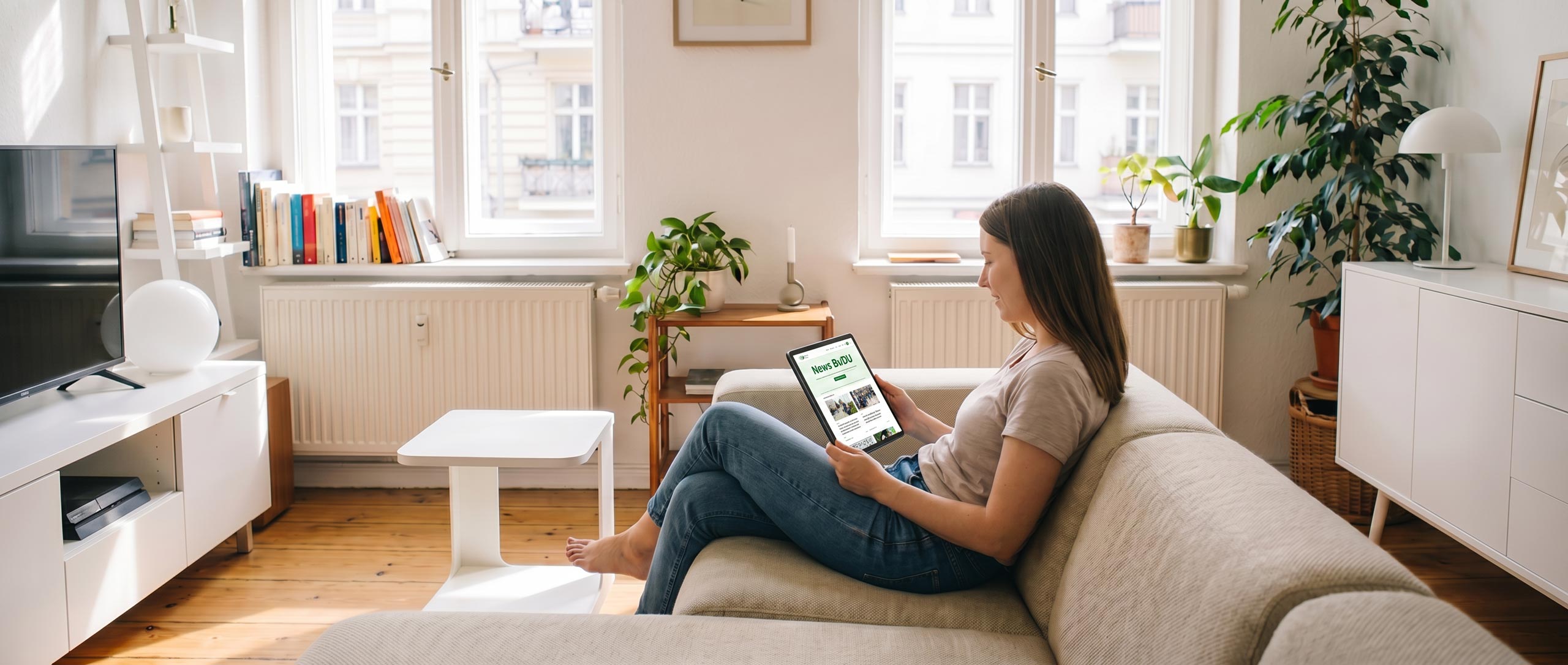 junge Ärztin sitzt zuhause auf sofa und schaut auf dem Tablet die News/Aktuelles vom BvDU